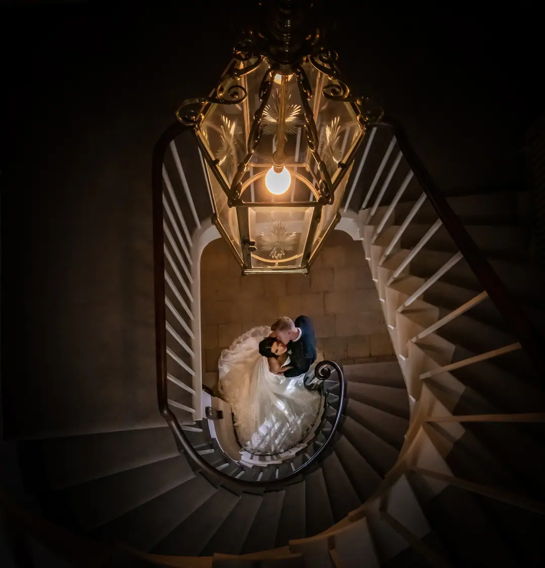 Looking down a spiral staircase at a couple beneath a chandelier