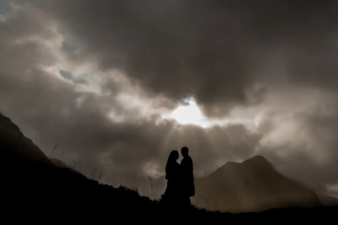 Couple silhouetted beneath a dramatic Highland sky