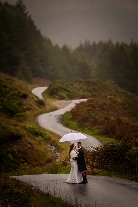 Couple beneath an umbrella on a winding Highland road