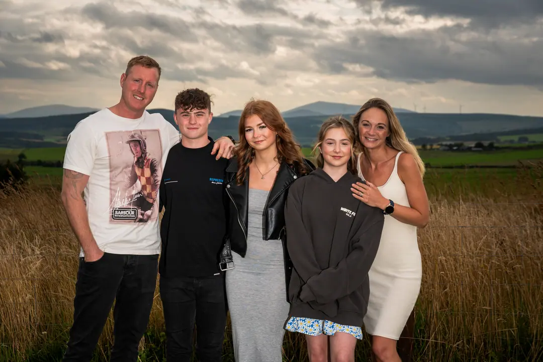 Family of five in a field with mountains behind