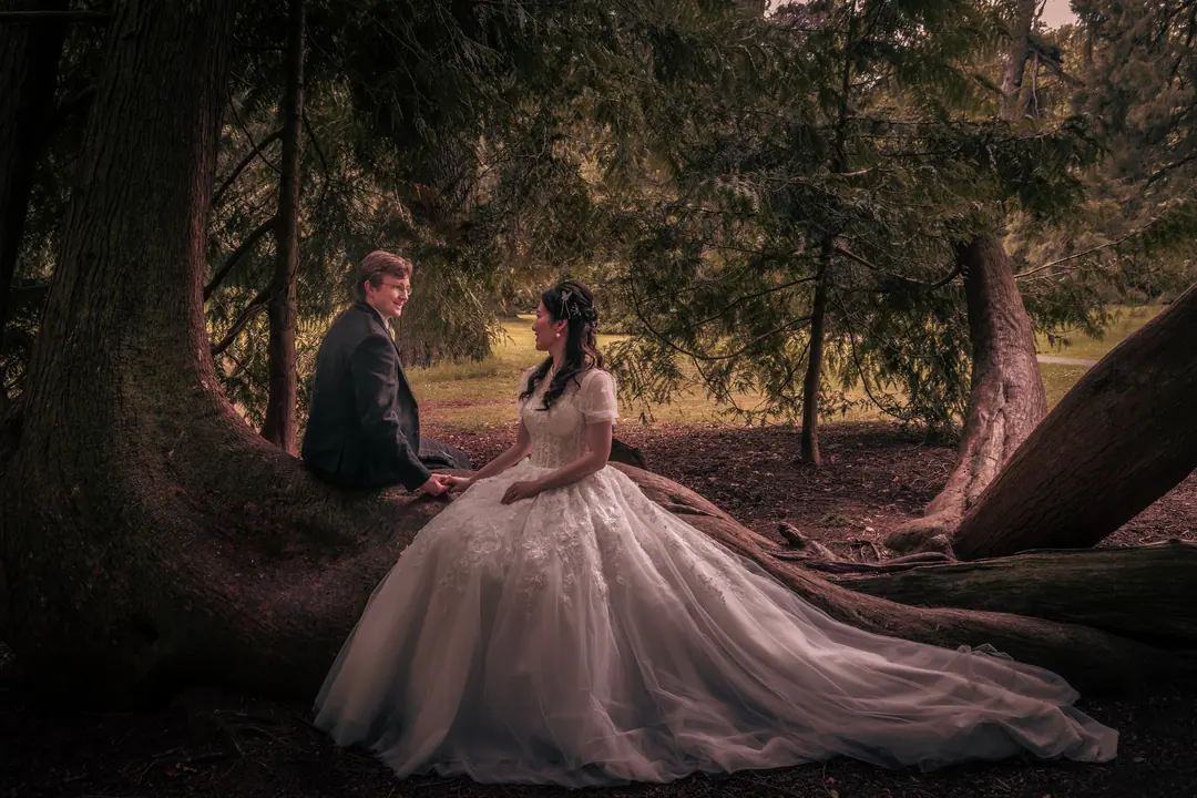 Bride in a flowing gown seated among ancient tree roots with her groom