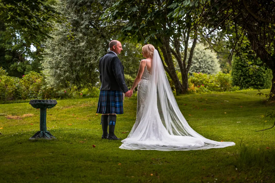 Groom in a kilt with his bride in a summer garden