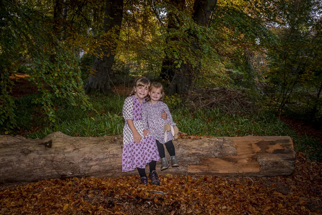 Two sisters seated on a fallen log in autumn woodland