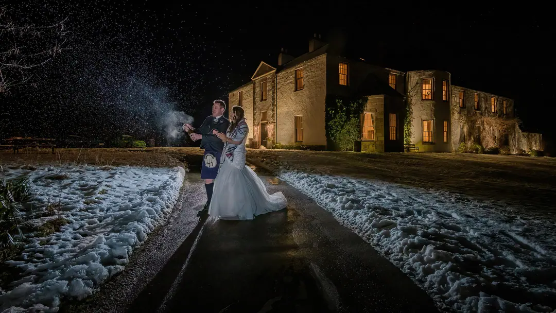 Bride and groom outside a floodlit country house at night