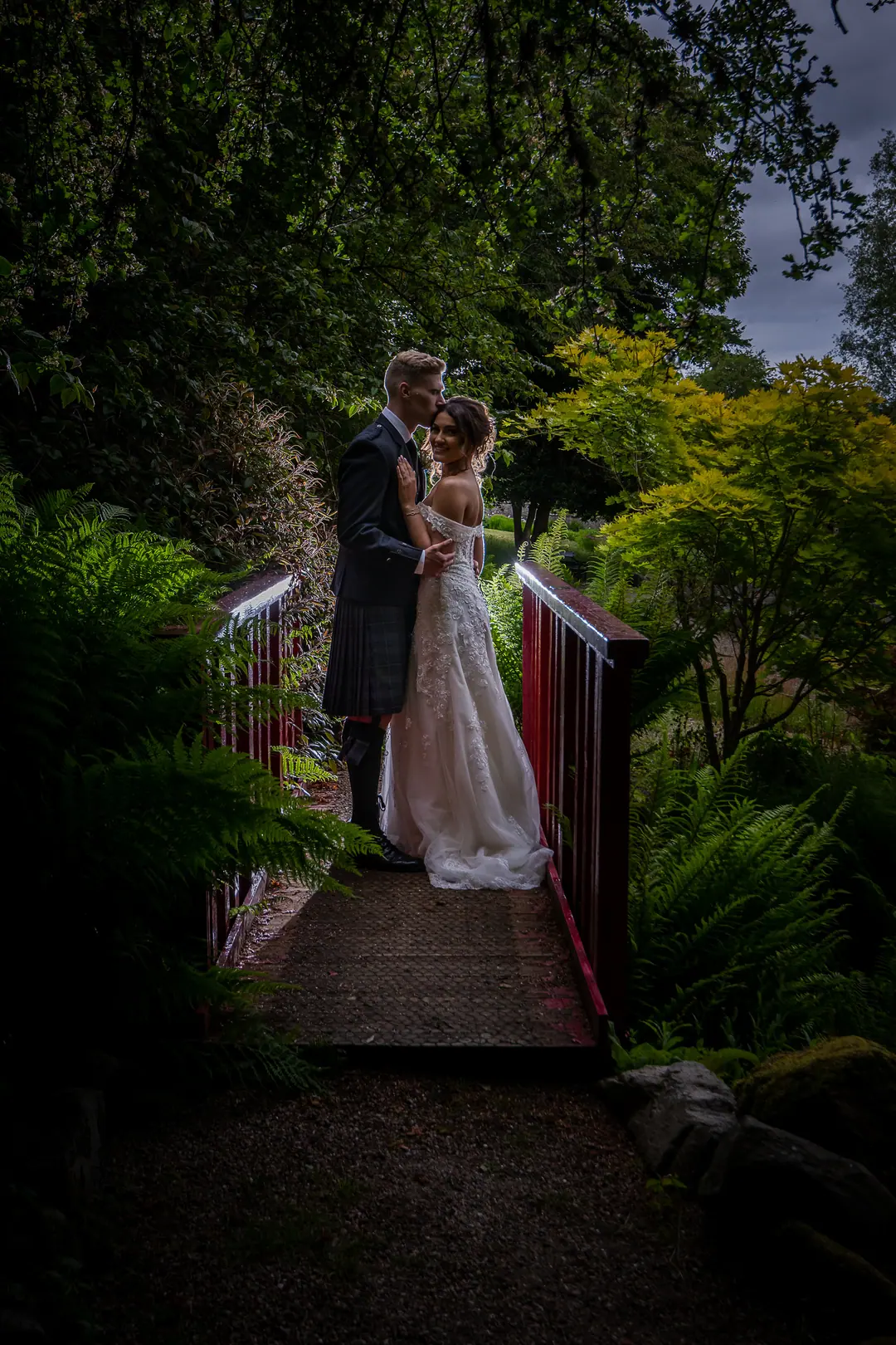Couple embracing on a red wooden bridge in lush woodland