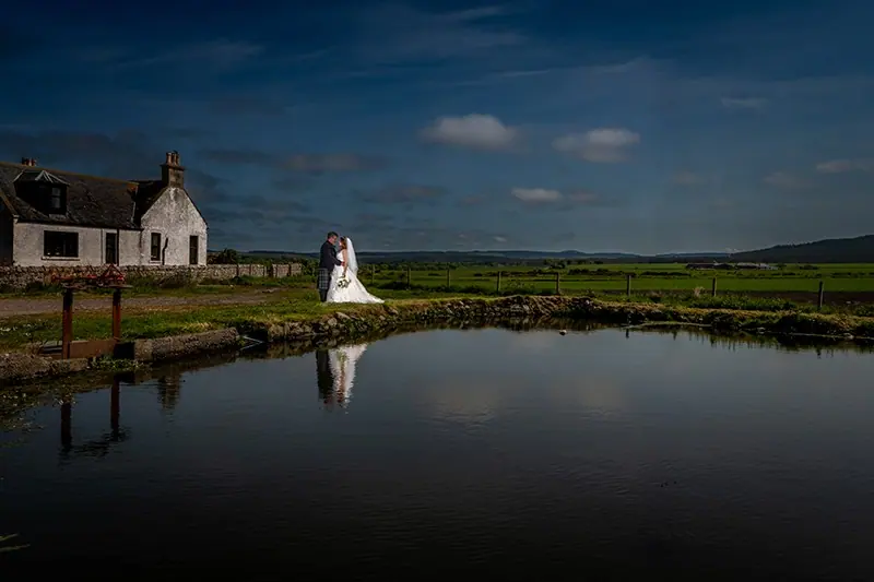 Couple reflected in a still pond beside a white house