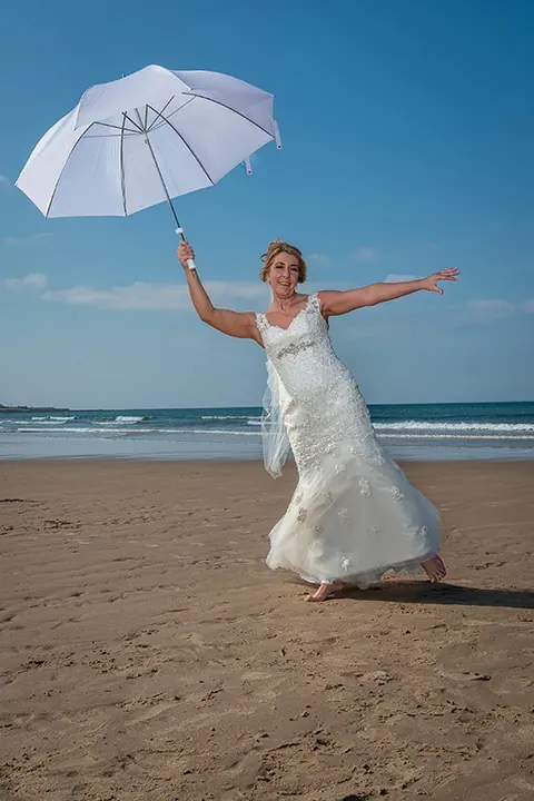Bride with a white umbrella on a sunny beach