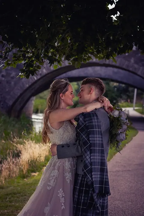 Couple beneath a lit arch at night, groom in tartan