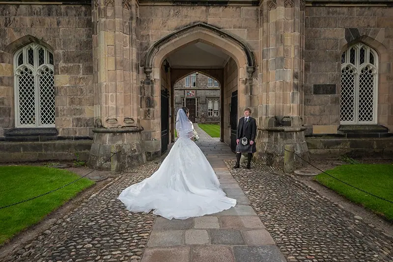 Bride's gown spread on cobbles before a gothic archway