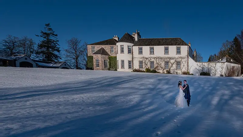 Couple on a snowy lawn in front of a white hotel
