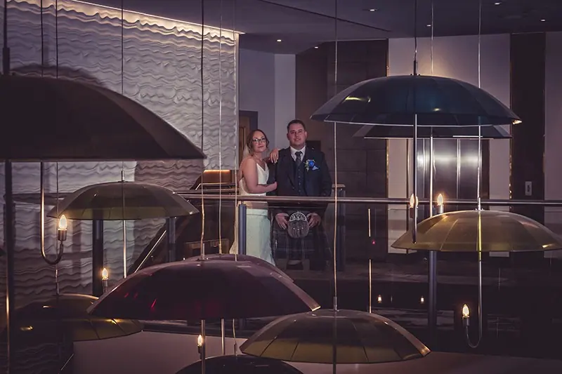 Couple beneath umbrellas at night beside illuminated lamps