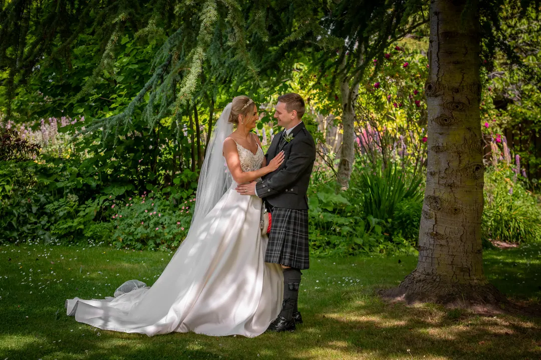 Groom holding his bride close in a sunlit woodland garden